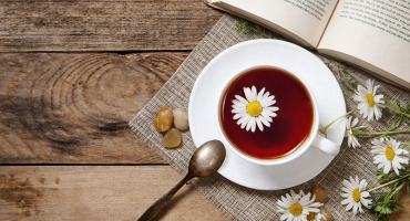 cozy cup of herbal tea with chamomile flowers and an open book on wooden table